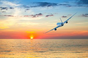 Jumbo jet airplane flying above tropical sea at beautiful sunset